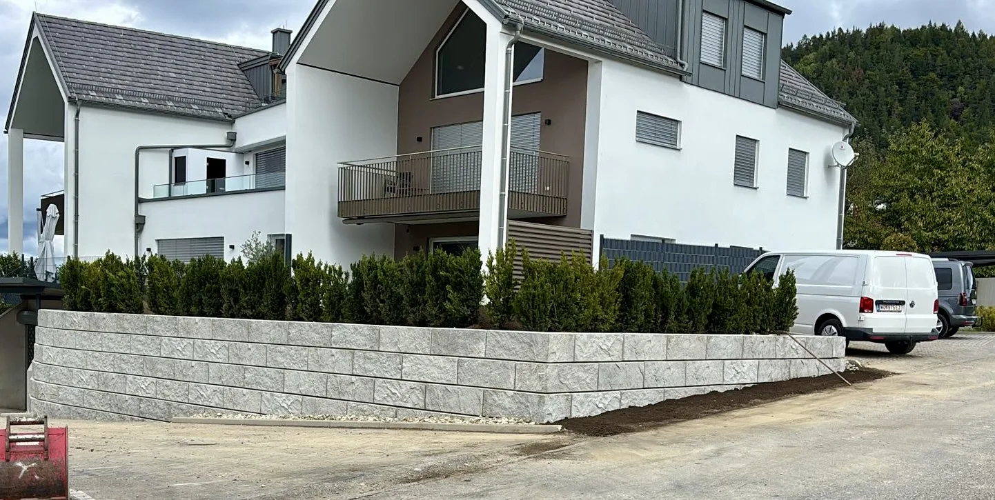Stützwand aus ZEMROCK Betonfertigteilen schafft zusätzliche ebene Fläche an einem Wohnhaus