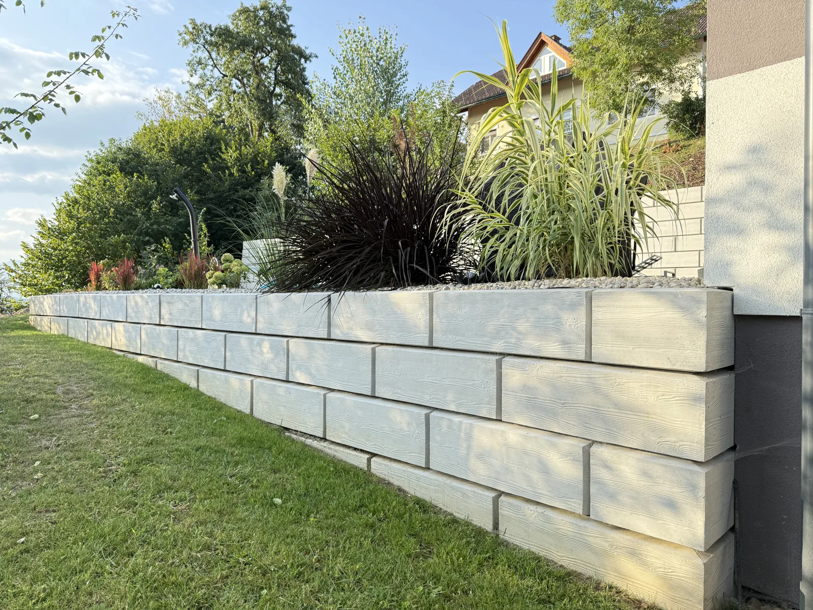 Niedrige Gartenmauer aus ZEMROCK Betonfertigteilen mit Bepflanzung als Teil einer Außenanlage